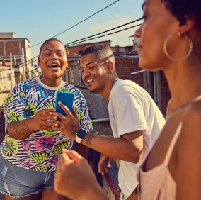 Duas mulheres e um homem ao ar livre sorrindo e olhando para celular