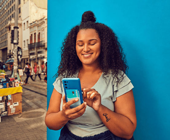 Mulher segurando celular e sorrindo em frente a fundo azul