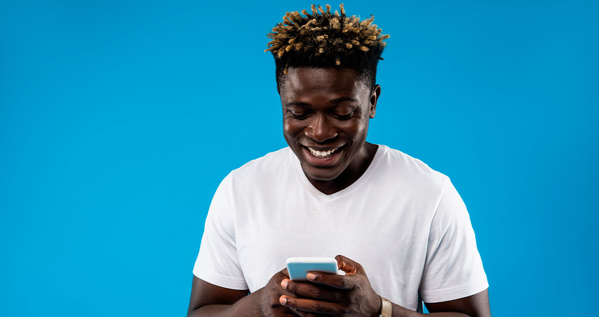 Homem em frente a fundo azul sorrindo e usando o celular