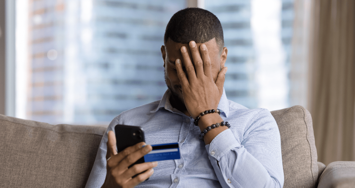 Homem segurando celular e cartão em uma mão e com a outra mão no rosto