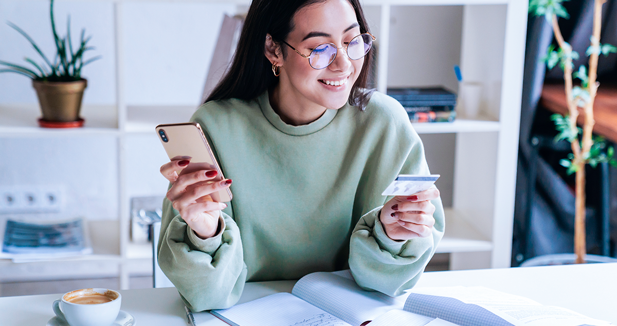Mulher segurando cartão de crédito em uma mão e celular em outra