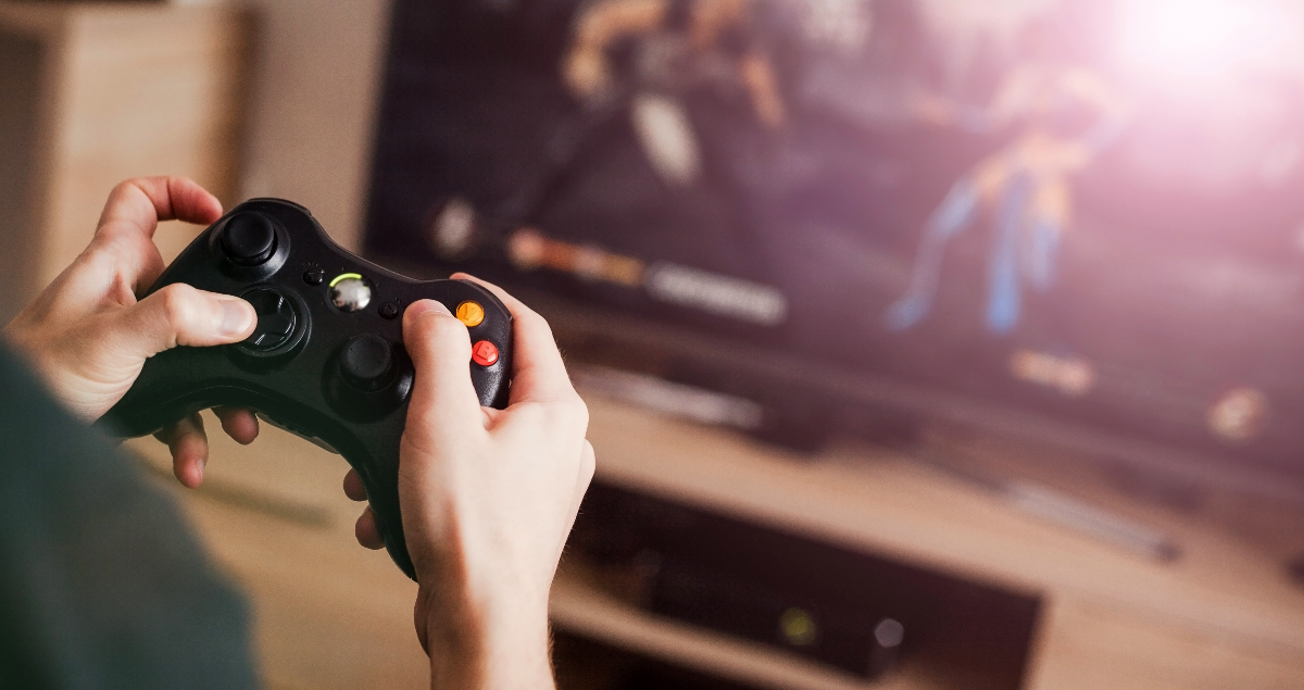 Pessoa segurando controle de videogame nas mãos em frente a televisão