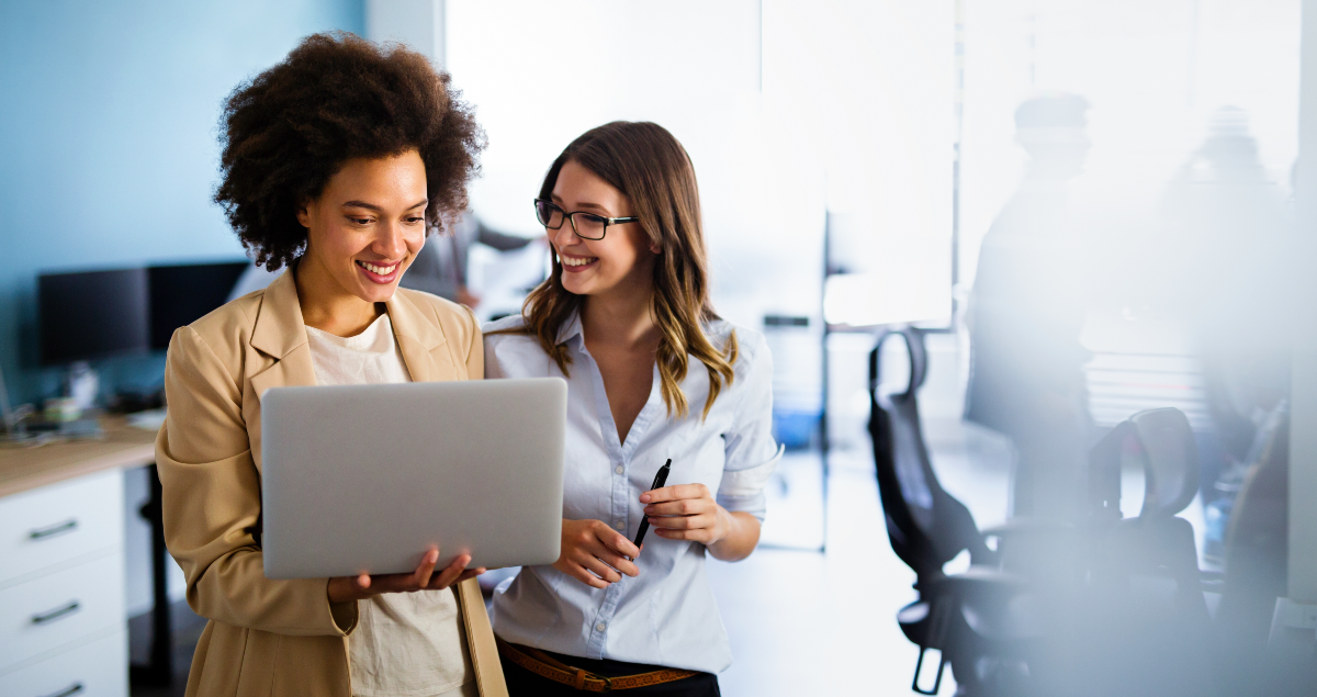 Duas mulheres em escritório olhando para computador e conversando