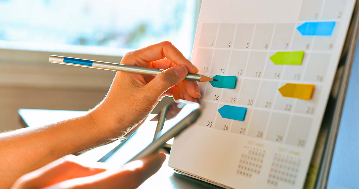 Pessoa com lápis em cima de calendário com etiquetas coloridas
