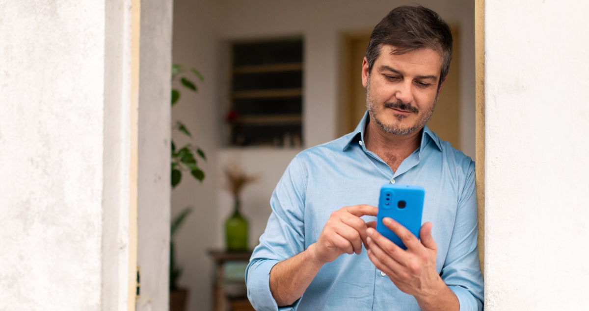 Homem mexendo em celular na porta de casa