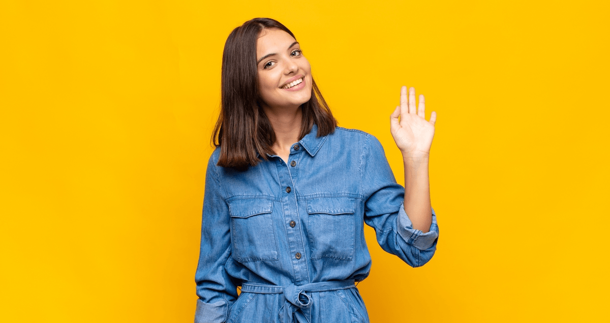 Mulher acenando e sorrindo em frente a fundo amarelo