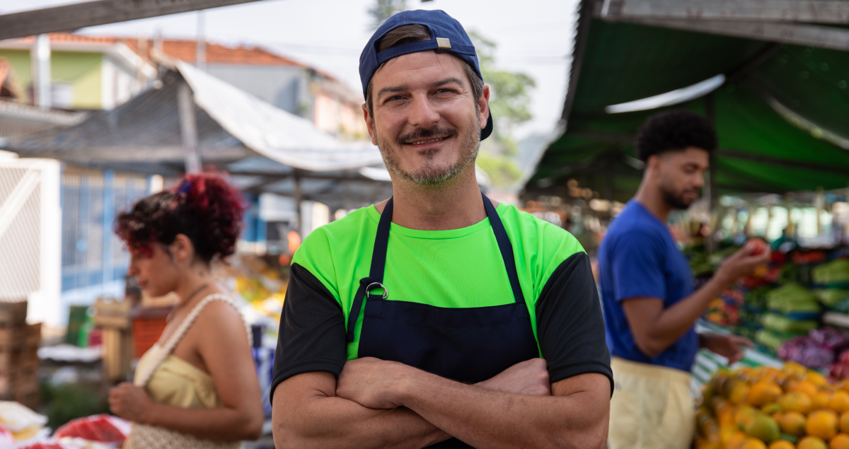 Homem de braços cruzados em feira e sorrindo