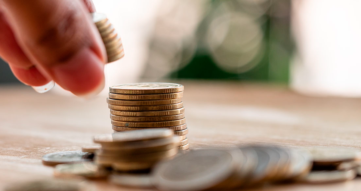 Pessoa colocando moedas em pilha de outras moedas