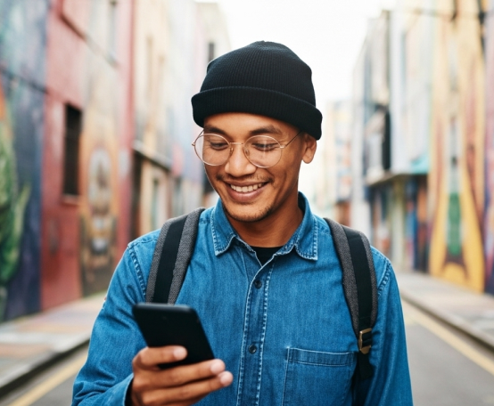 Homem sorrindo, segurando e olhando para o celular.