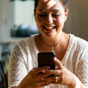 Mulher na rua sorrindo e mexendo em celular