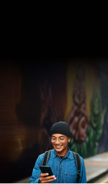 Homem ao ar livre com mochila nas costas e fone de ouvido segurando o celular na mão