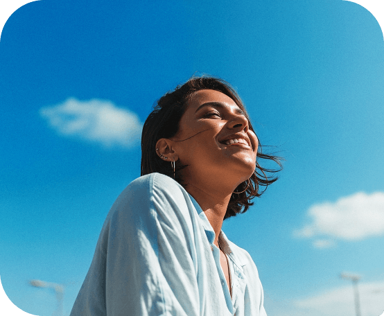 Mulher sorrindo olhando para o céu em um dia ensolarado, transmitindo sensação de liberdade e bem-estar