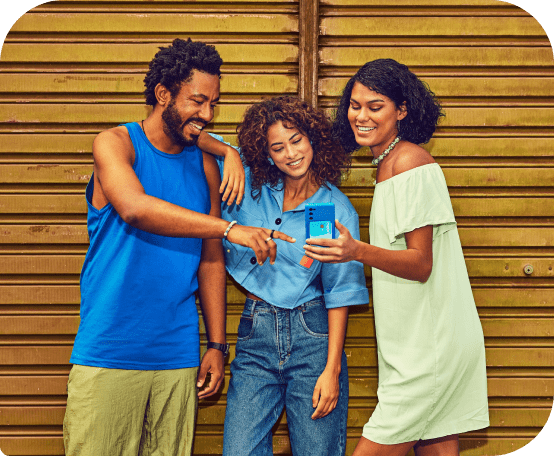 Um homem e duas mulheres em frente a portão amarelo, todos olhando para um celular