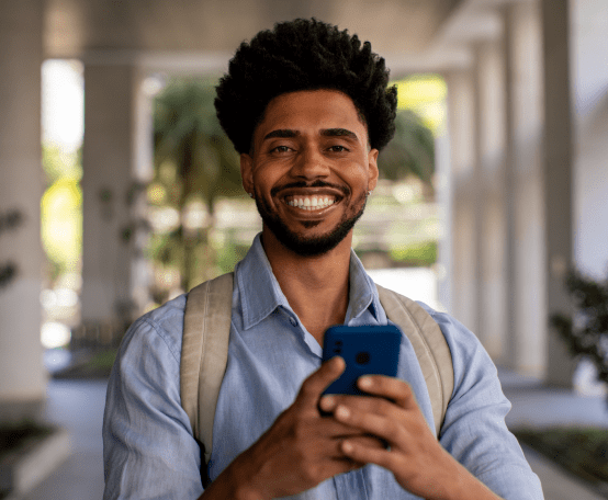 Homem de mochila sorrindo segurando celular nas mãos