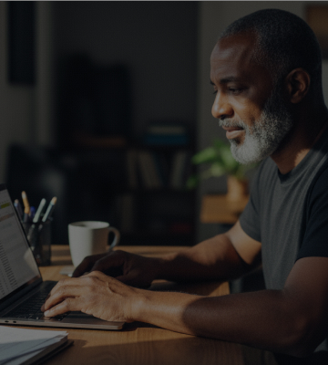 Homem trabalhando em um notebook em luz iluminando parte do seu rosto