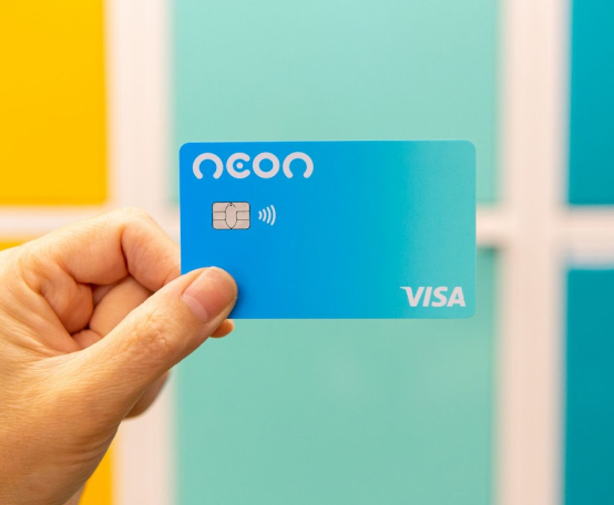 Viracrédito: Mão segurando cartão de crédito Neon em frente a fundo colorido