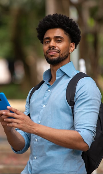 Homem de mochila nas costas sorrindo segurando celular